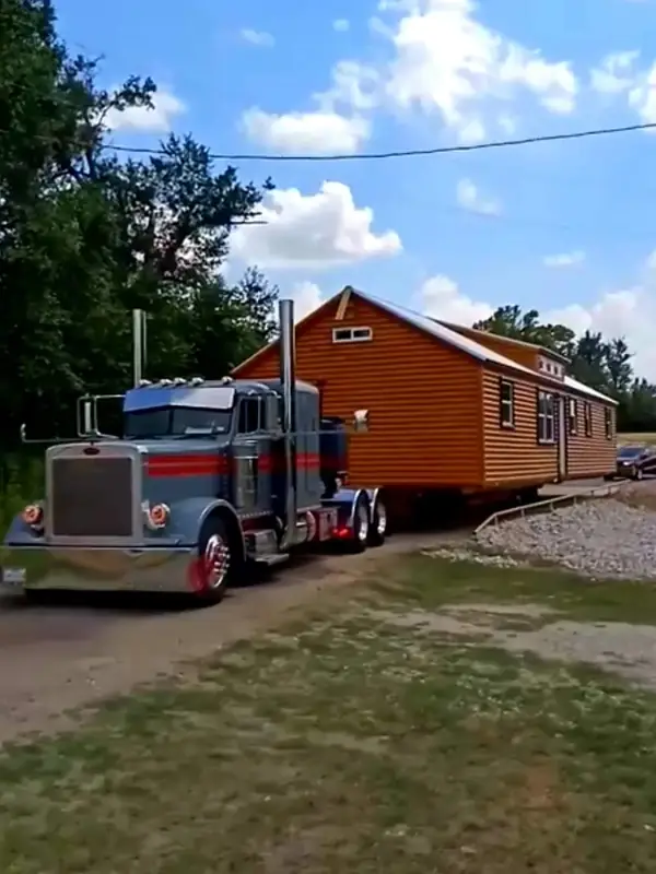 A semi truck hauling a finished cabin down a country road